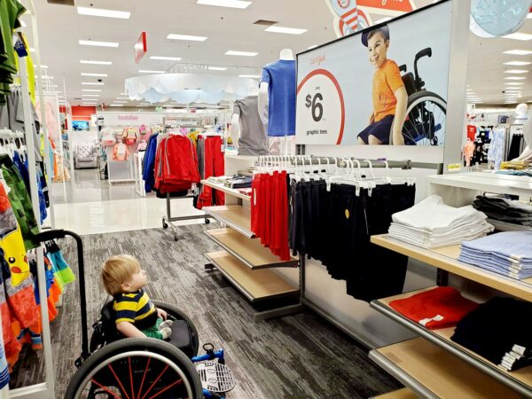 An image of a disabled child named Ollie sitting in his wheelchair and looking up adorably at an ad inside Target of another boy in a wheelchair.